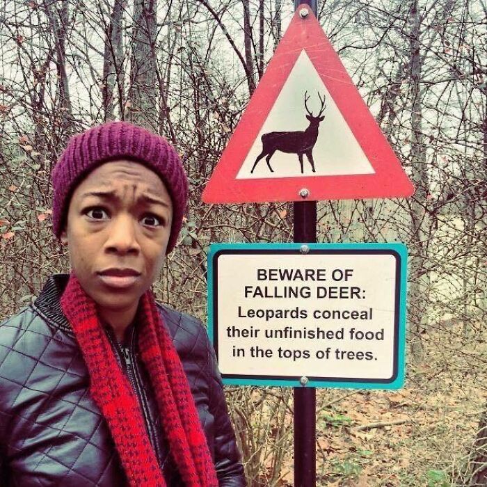 Woman looking surprised beside a strange warning sign about falling deer and leopards concealing food in trees.