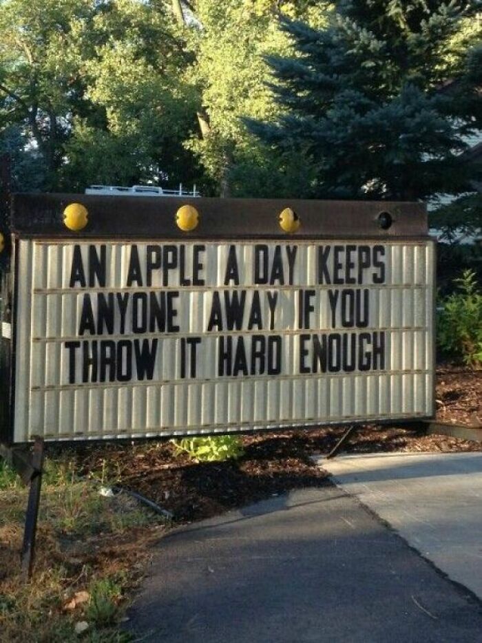 Humorous strange sign outdoors with the message about an apple keeping people away if thrown hard enough.