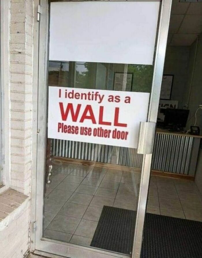 Sign on glass door reads I identify as a wall please use other door, an example of strange signs to double take.
