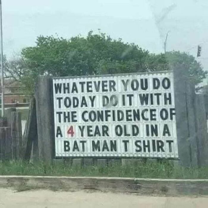Strange sign encouraging confidence by comparing actions to a 4-year-old wearing a Batman shirt outdoors.