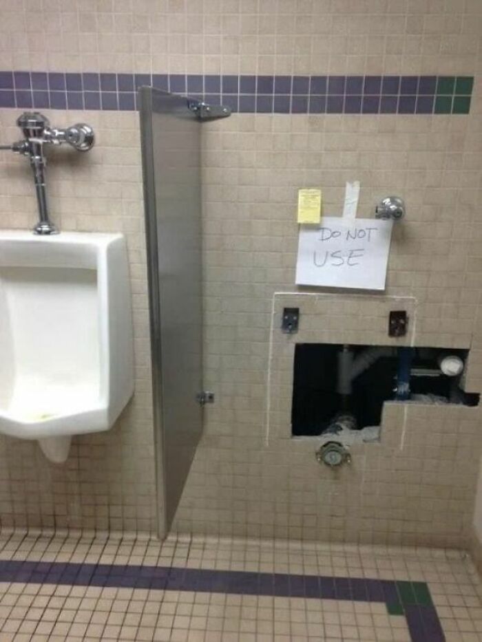 Restroom scene with a urinal next to a strange broken wall and a handwritten do not use sign taped above it.