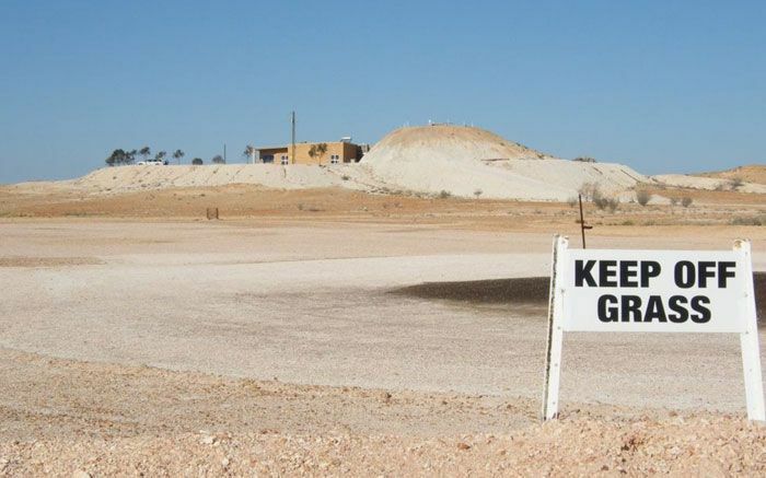 Sign reading keep off grass placed in a barren, dry landscape with no visible grass, showcasing strange signs.