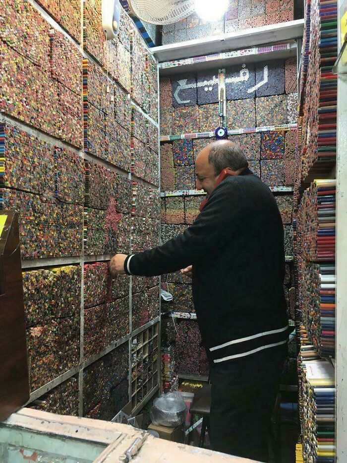 A man in a narrow room filled with thousands of colorful crayons, reaching for one. An amazing photo of unique storage.