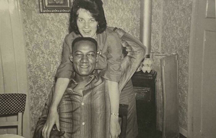 Candid old photos: A smiling couple, a woman embracing a man from behind, in a cozy indoor setting.