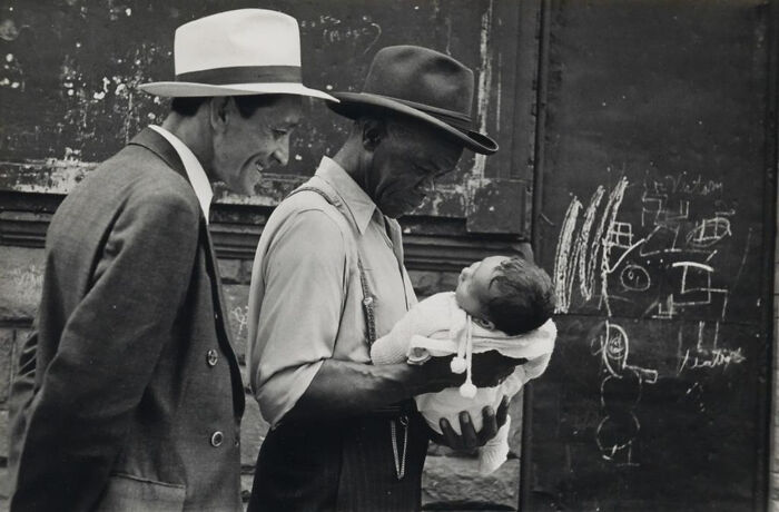 Candid old photos: Two men in hats admiring a baby carried by one, street with chalk drawings on a wall.