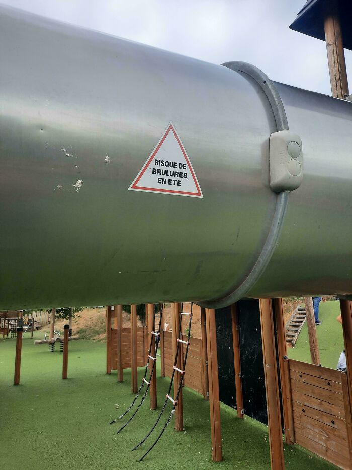 Large metal playground slide with a burn risk warning label, illustrating terrible product design safety issues.