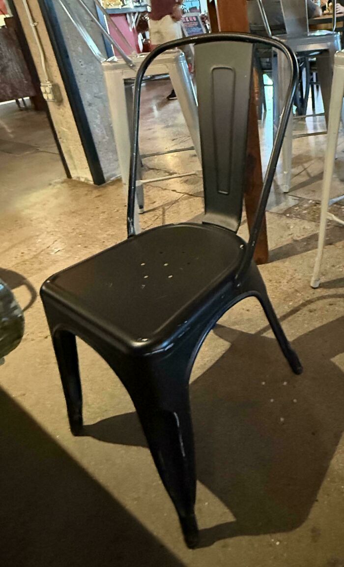 Black metal chair with a broken backrest design, an example of terrible product designs in a café setting.