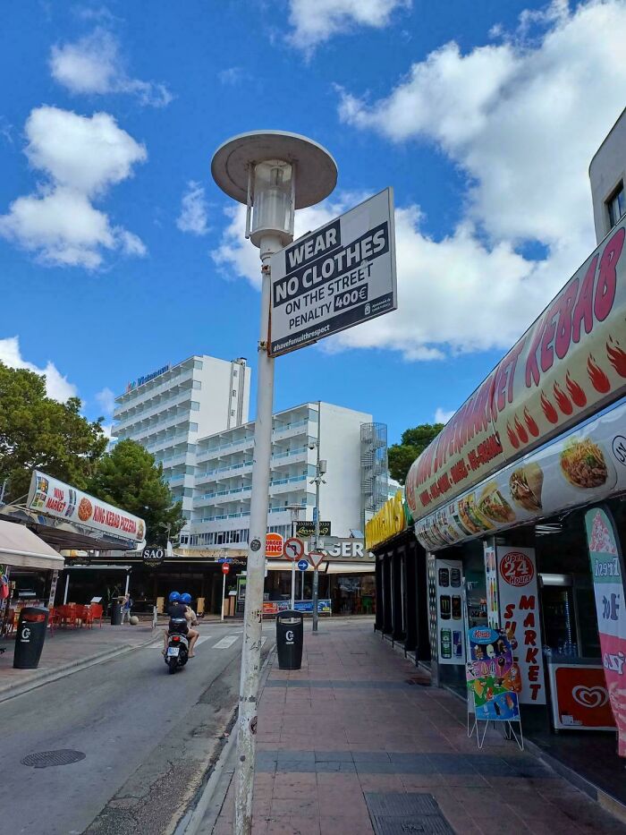 Street scene with a sign showing a confusing product design about clothing rules and penalties in a public area.