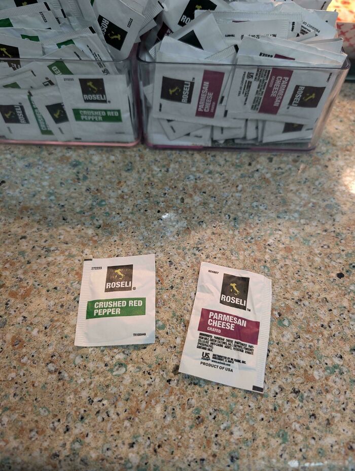 Packets of crushed red pepper and grated Parmesan cheese on a cluttered countertop with poor product design.