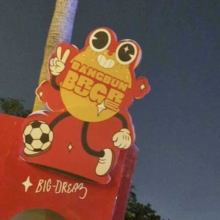 Sign featuring a cartoon character with big eyes holding a peace sign, illustrating terrible product designs outdoors at night.