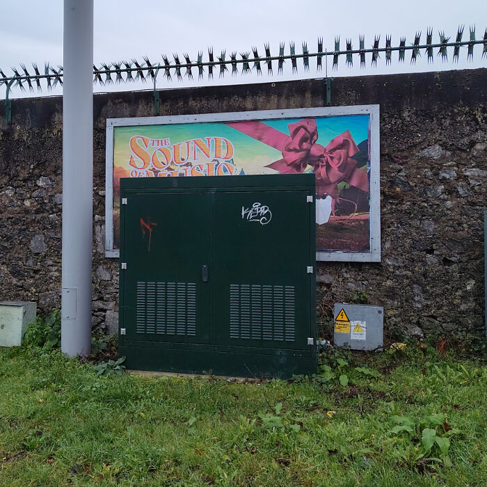 Green utility box blocking a colorful outdoor advertising billboard, illustrating terrible product design placement.