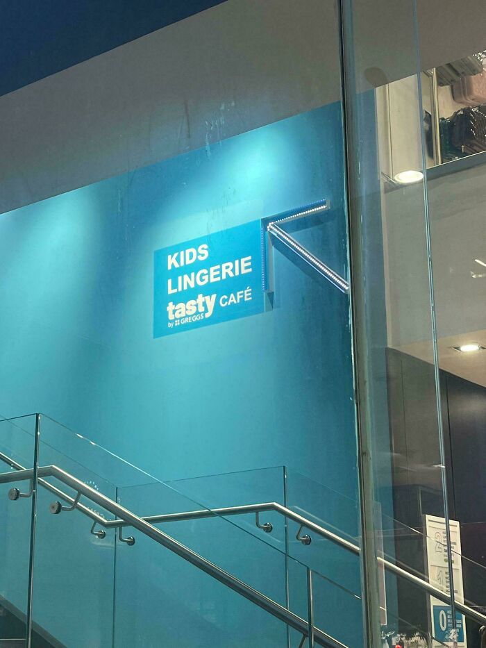 Sign with confusing product design reading kids lingerie tasty café displayed on blue wall by staircase.