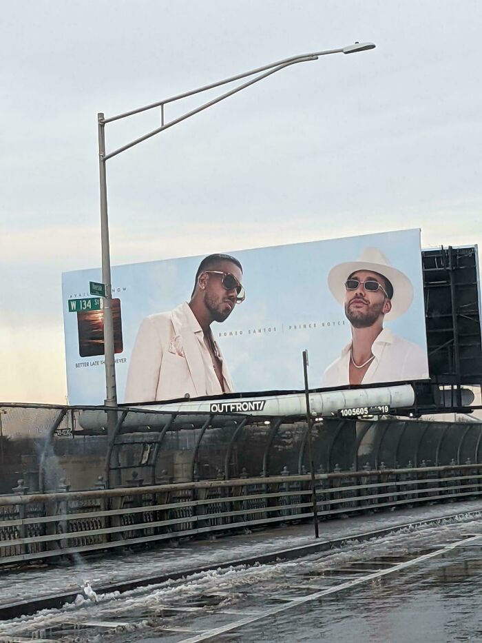 Billboard with two men wearing sunglasses and hats, featuring a terrible product design obstructing the street sign.