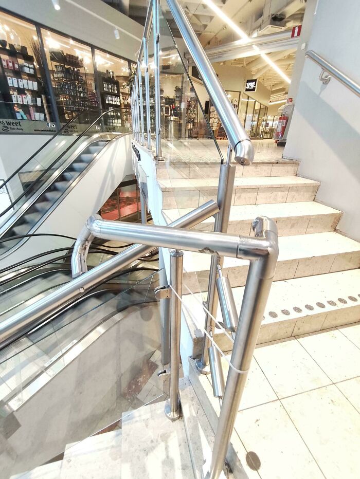Metal handrail with a sharp bend blocking access to stairs, illustrating terrible product design flaws in public spaces.