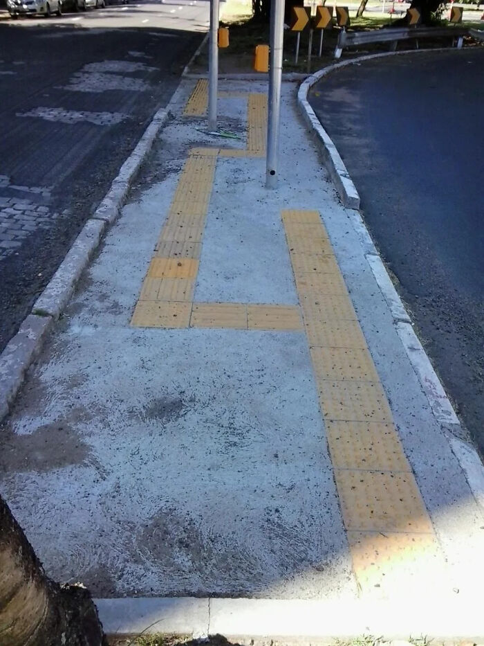 Sidewalk with tactile paving designed for the visually impaired blocked by metal poles, a terrible product design fail.