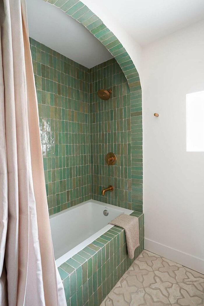 A bathroom with a bathtub surrounded by green subway tiles and a light-colored shower curtain, a refreshing home decor project.