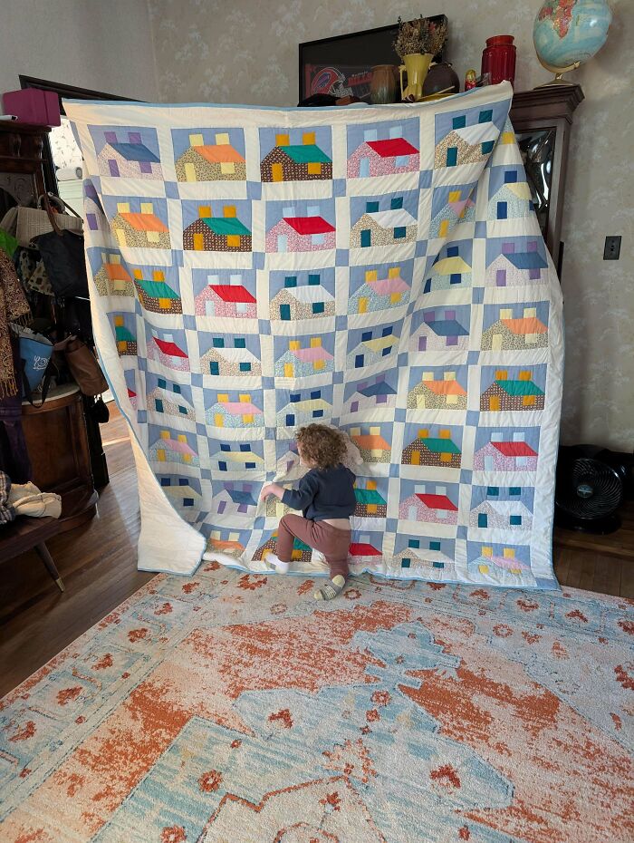 A child peeking from behind a large, colorful house-patterned quilt, a lucky dumpster diving discovery.