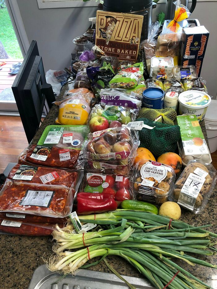 A kitchen counter overflowing with various grocery items like meats, produce, and packaged goods, showcasing successful dumpster diving.