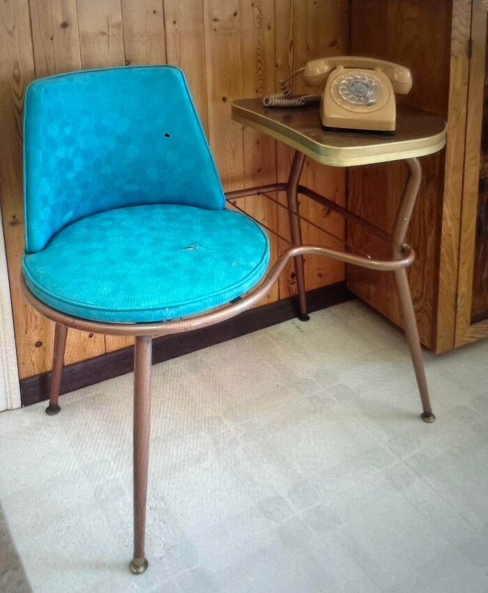 A vintage teal chair with an attached small table holding an old rotary phone, a unique dumpster diving find.