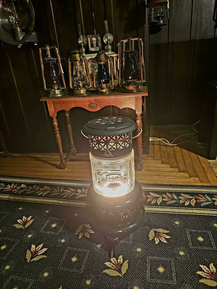 A glowing vintage kerosene heater on a patterned rug, with several antique lanterns displayed on a wooden table in the background. Buy It For Life purchases.