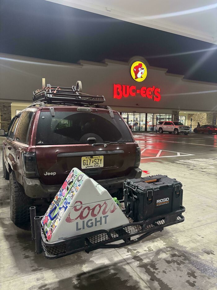 A maroon Jeep with a roof rack and cargo carrier with a Coors Light cooler and Ridgid box, parked outside Buc-ee's at night. These are Buy It For Life purchases.