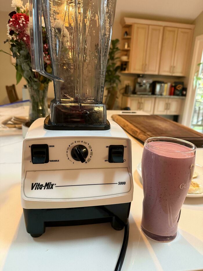 A white Vita-Mix 5000 blender with a purple smoothie in a glass, a Buy It For Life purchase, in a kitchen.
