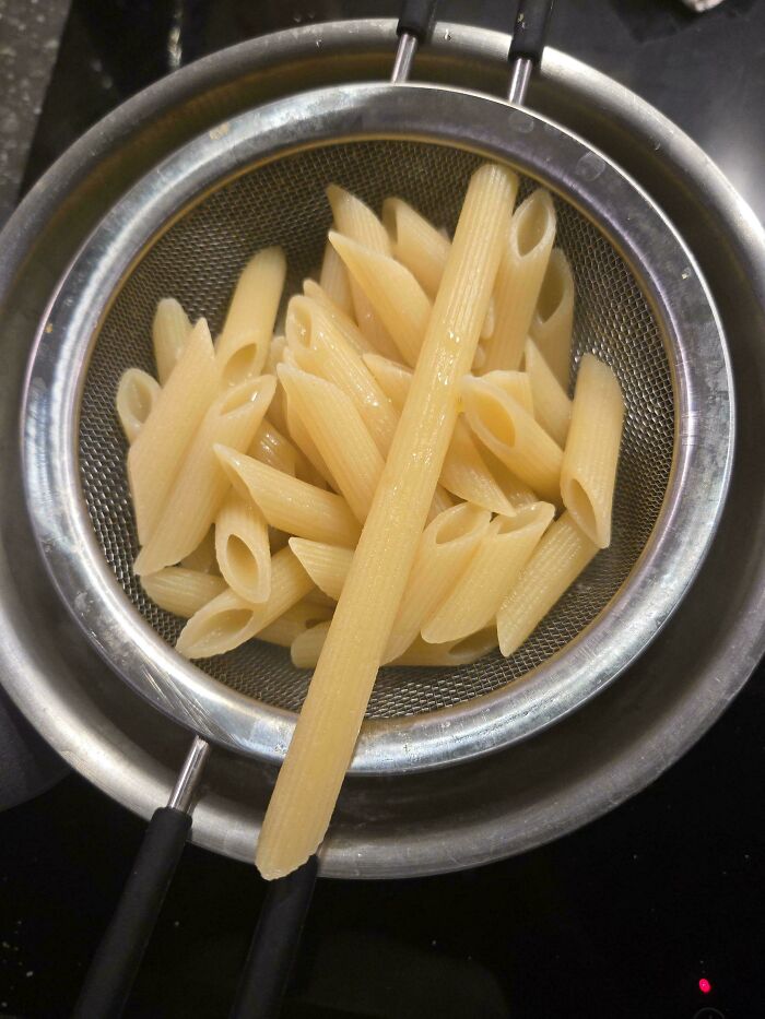Cooked penne pasta draining in a metal colander over a pot, capturing a mildly interesting picture of the cooking process.