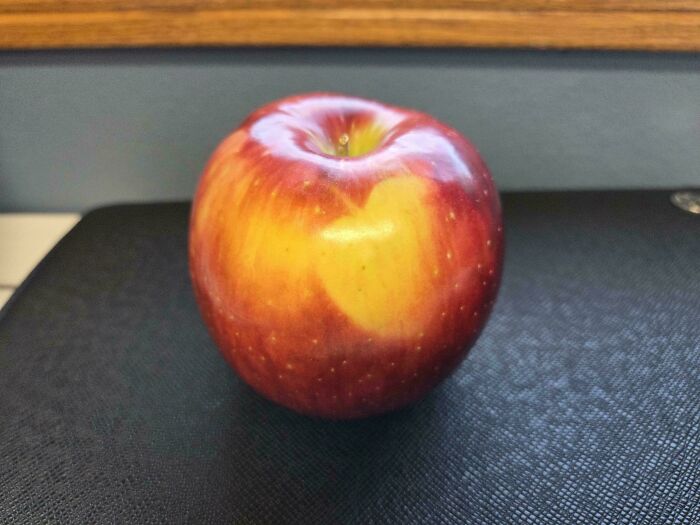 A vibrant red and yellow apple sits on a dark surface, showcasing its unique coloring in a mildly interesting picture.