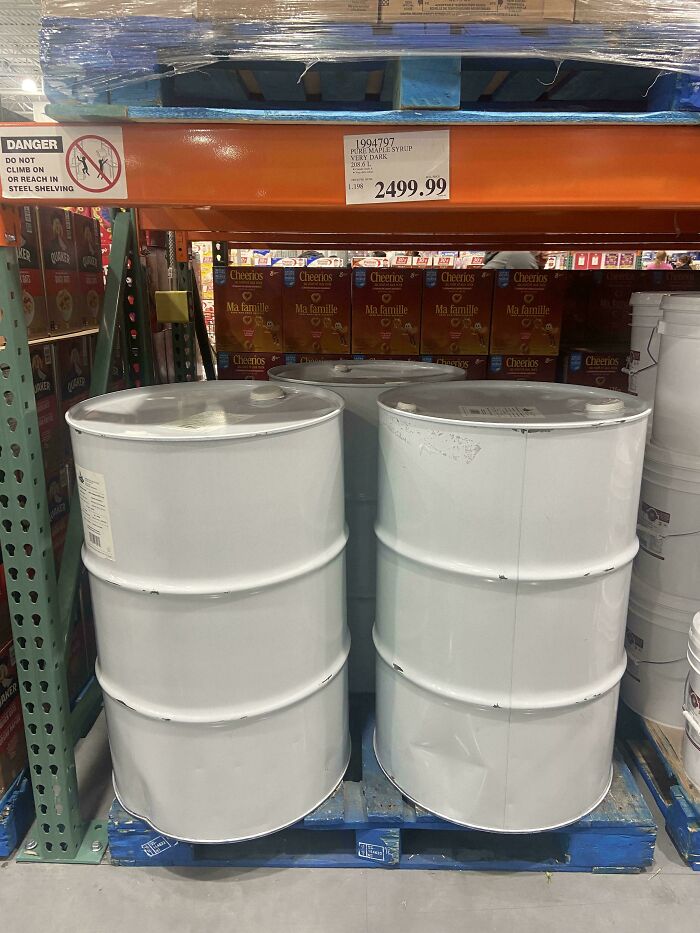 Two large white barrels on a pallet beneath shelves of cereal boxes and a price tag in a warehouse, making for mildly interesting pictures.