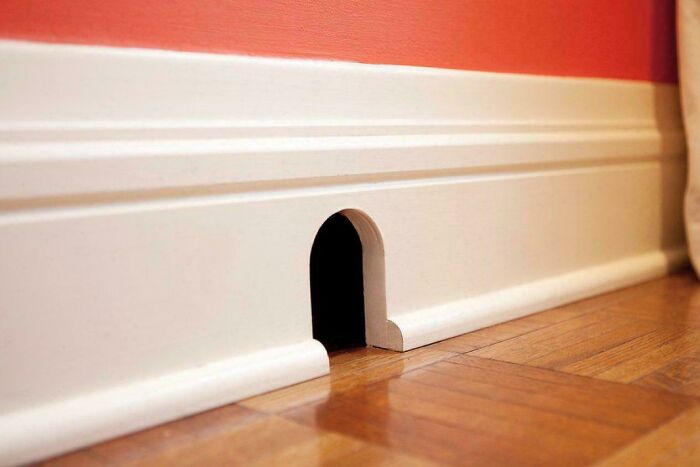 A small, arched mouse hole in a white baseboard against a red wall, a picture made of online lies.