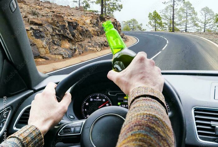 Hands on a steering wheel, one holding an open green beer bottle, depicting dangerous online lies on the road.