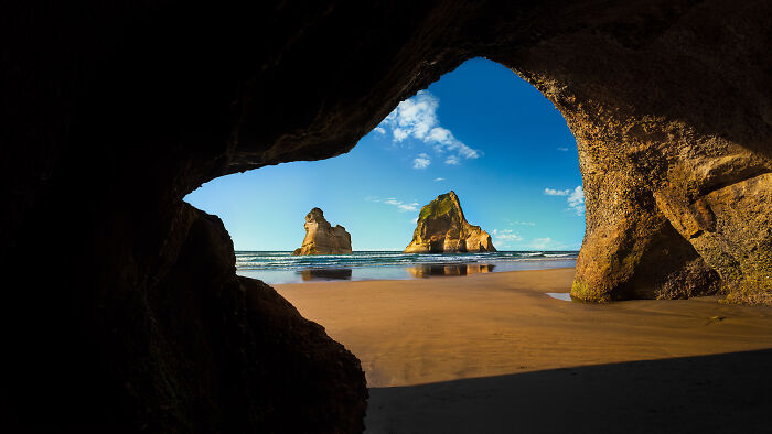 A beautiful beach scene with large rock formations, viewed from inside a cave, not related to online lies.