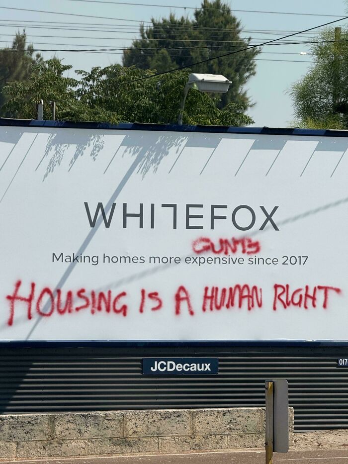 Billboard vandalized with housing protest graffiti in urban area