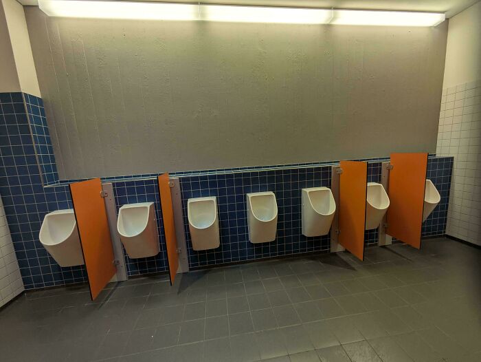 Row of urinals with poorly placed privacy dividers in public restroom