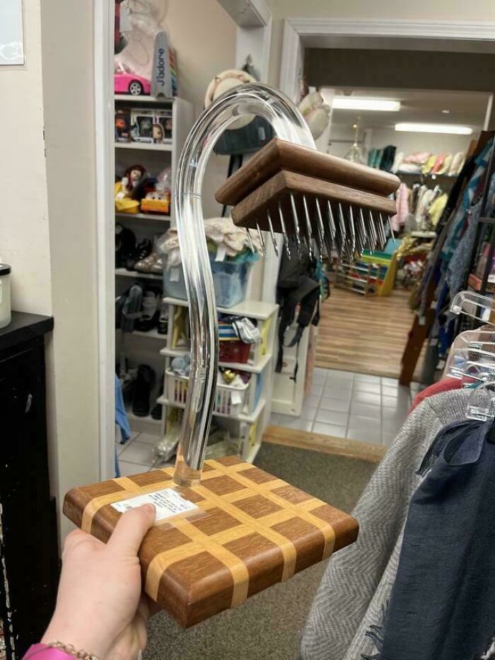 Hand holding a strange wooden and metal object with spikes, appearing confusing and unusual in a cluttered room setting.