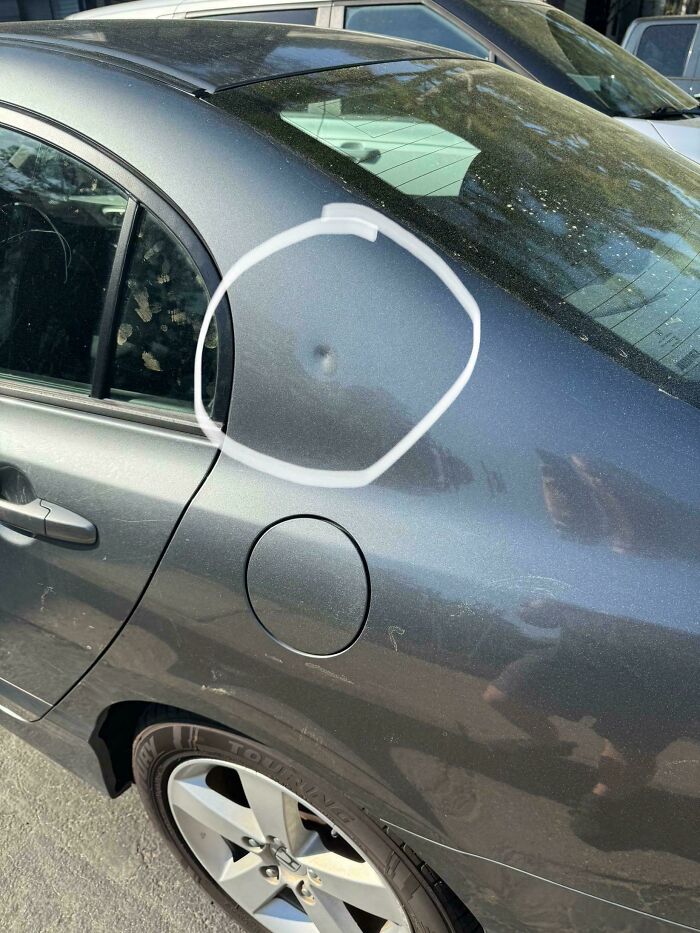 Car dent circled in white on a dark gray vehicle, showing a strange and confusing damage spot.