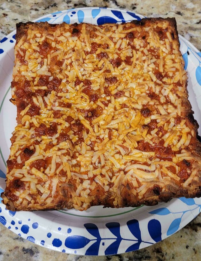 Square-shaped pizza slice with unevenly melted cheese on a paper plate, a strange pic that people just had to take