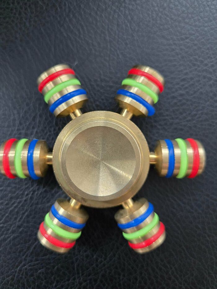 Strange pic of a metal fidget spinner with colorful rubber rings on black textured background, causing utter confusion.