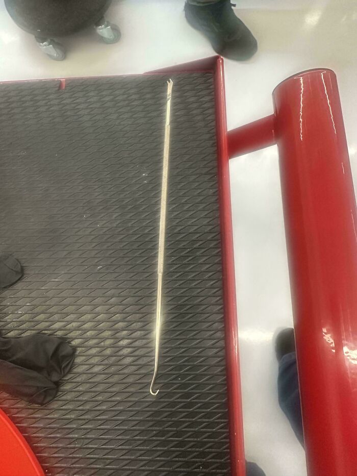 Long strange object with a hook end placed on a textured black surface, captured in a confusing setting.