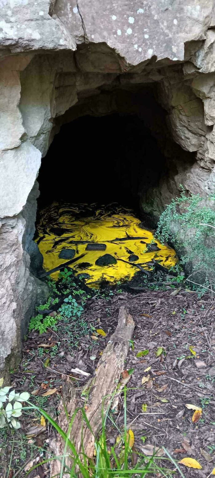 Dark cave entrance with strange yellow substance and scattered rocks, a bizarre and confusing natural scene.