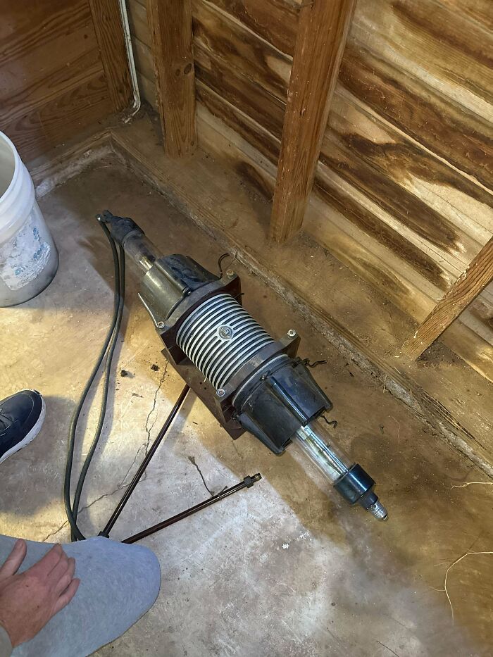 Unusual mechanical device with cables and glass tube on concrete floor inside wooden shed, strange pics concept.