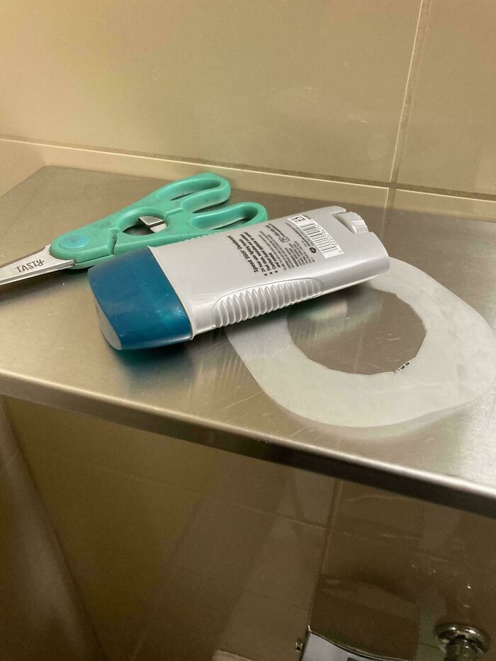 Scissors, deodorant, and a cut-out tape circle on a shiny metal bathroom shelf in a strange pics collection.