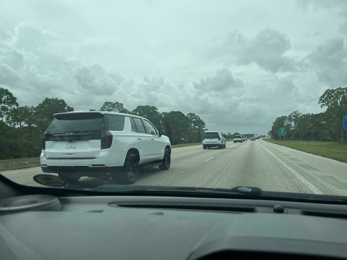 White SUV on the highway captured from inside another vehicle, showcasing a strange scene on the road with overcast skies.