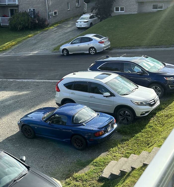 Blue convertible car oddly parked on gravel next to neatly lined SUVs, a strange pic that captures confusion in parking choices.