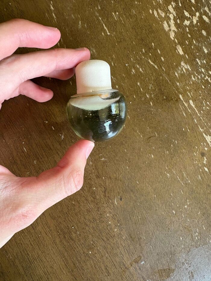 Hand holding a small round glass container with a white stopper, one of the strange pics causing utter confusion.