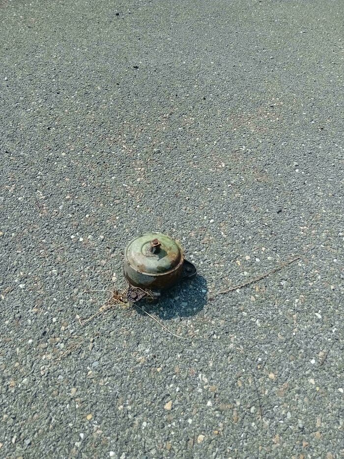 Rusty metal object stuck in asphalt pavement creating a strange pic that leaves people utterly confused on the street.