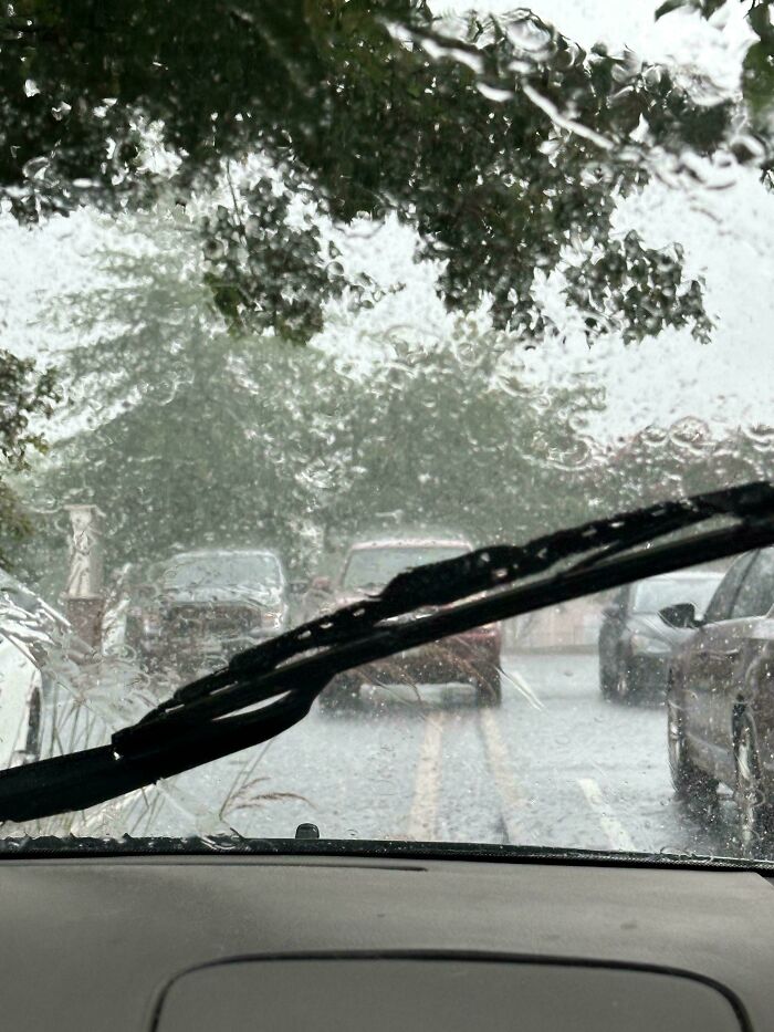 View through rain-soaked car windshield with wiper moving on strange pics causing confusion in traffic scene