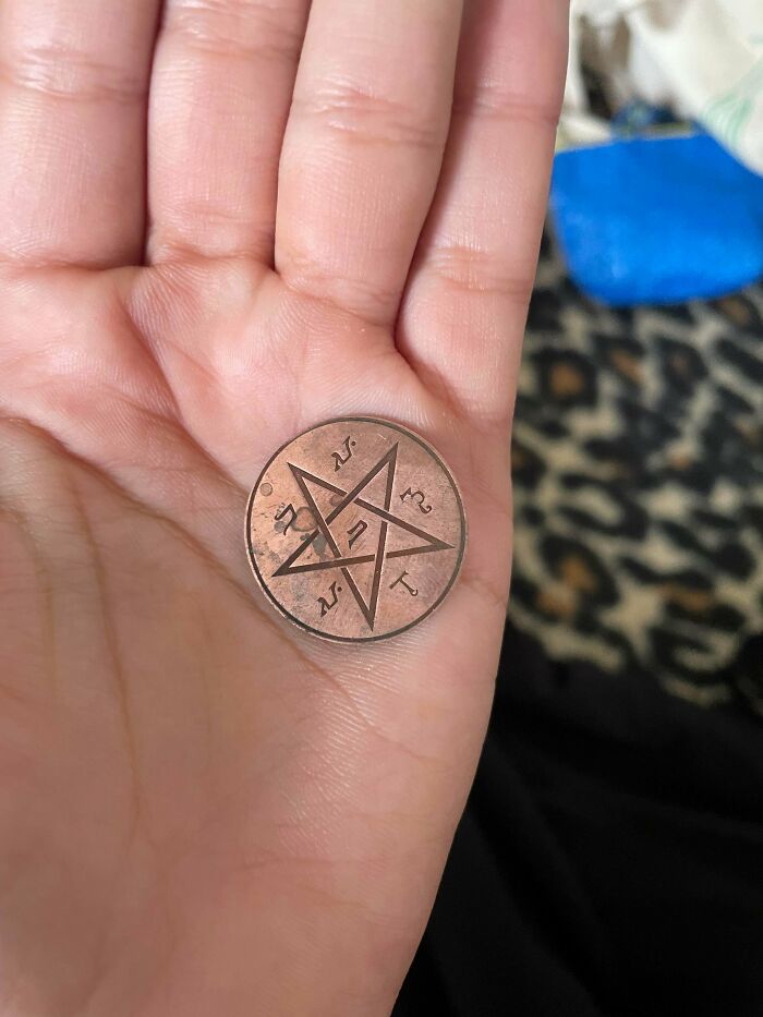 Hand holding a coin with a strange pentagram design, one of the strange pics that people just had to take out of confusion.