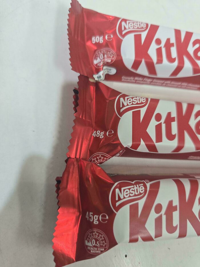 Three Nestle KitKat bars with decreasing weights of 50g, 48g, and 45g illustrating obvious shrinkflation impact.