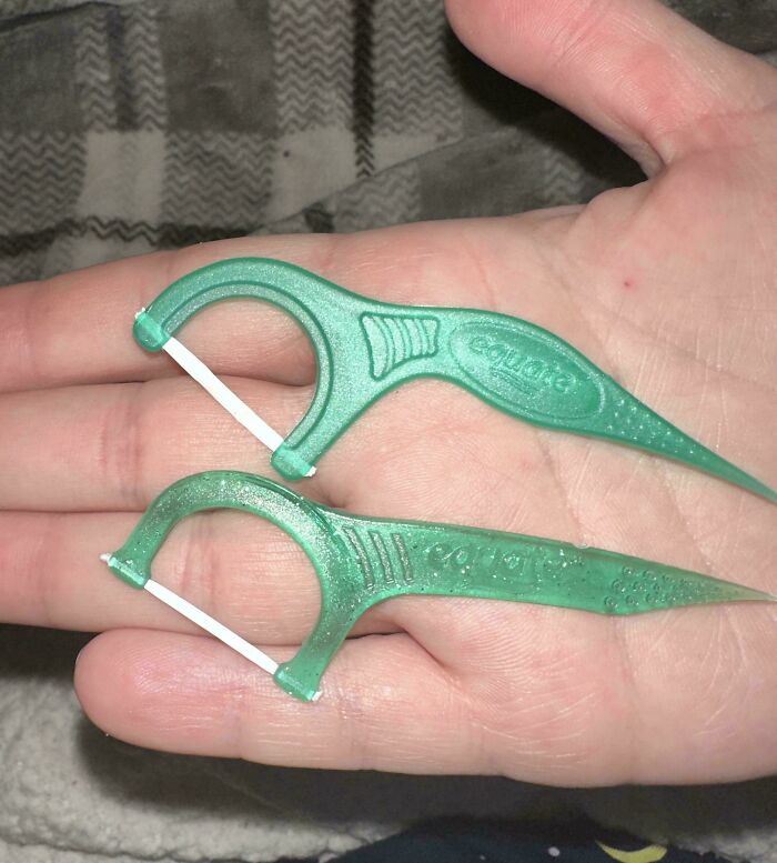 Two green plastic floss picks in a hand showing obvious shrinkflation as part of an America consumer trend.